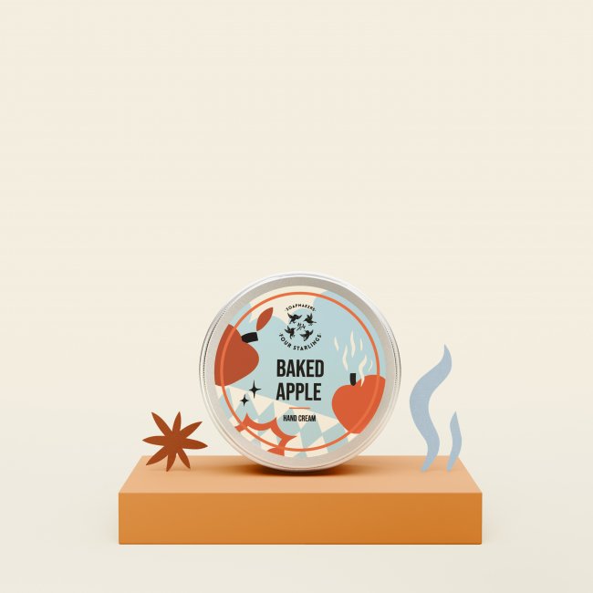 Okrągła puszka z napisem Pieczone Jabłko z ilustracjami jabłek i przypraw znajduje się na pomarańczowym podeście, w towarzystwie papierowych wycinanek gwiazdek anyżu i niebieskich kształtów dymu na jasnobeżowym tle.